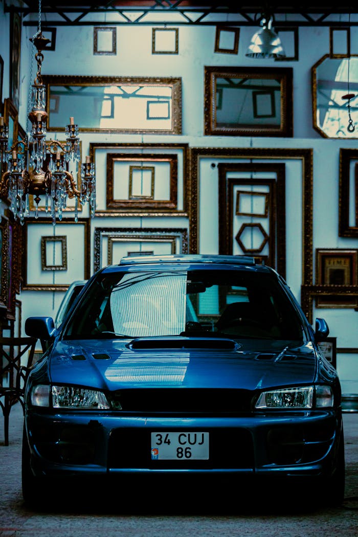 A vintage blue Subaru car parked inside a frame-filled gallery, showcasing unique automotive style.