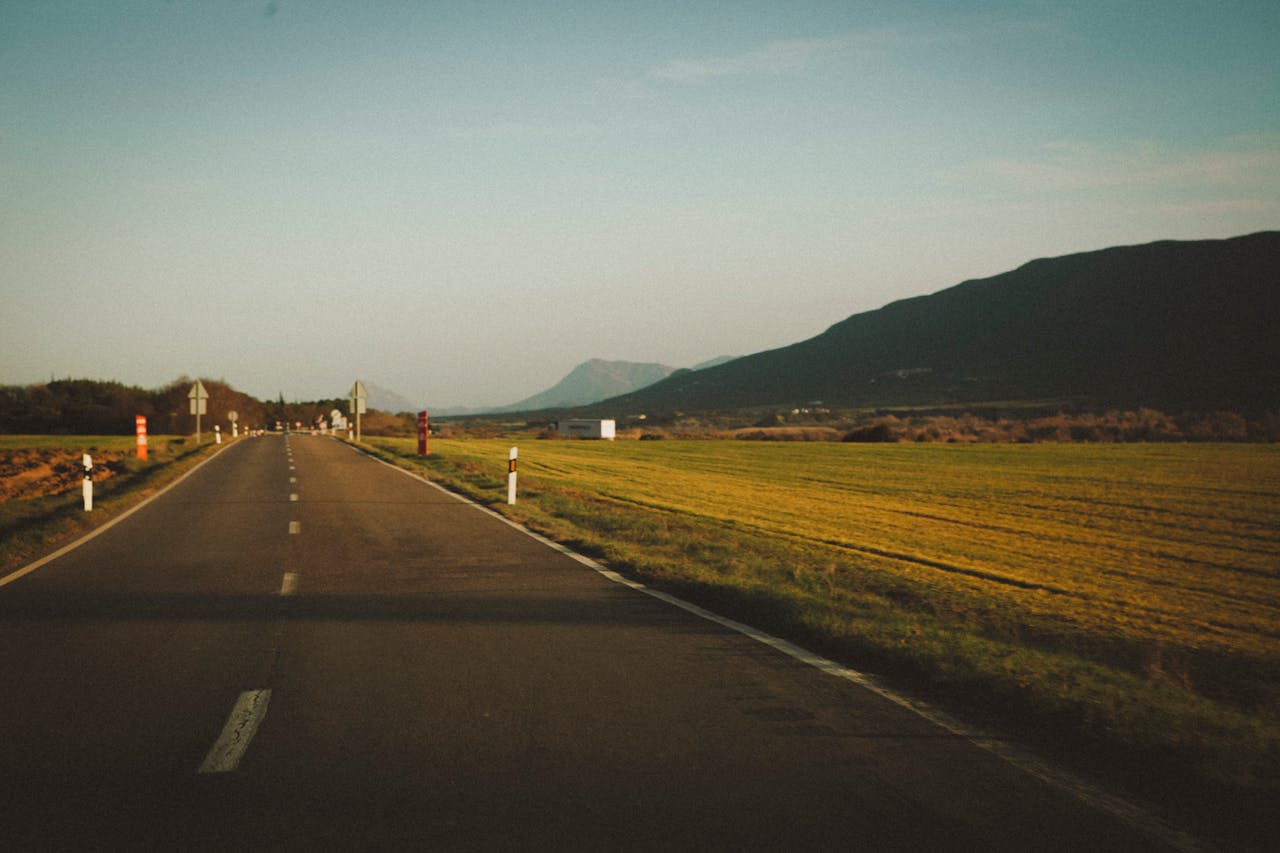 A tranquil rural road with fields and mountains in the scenic countryside during sunset.
