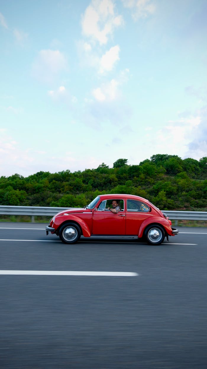 A classic red Volkswagen Beetle driving on a highway in İstanbul, Turkey.