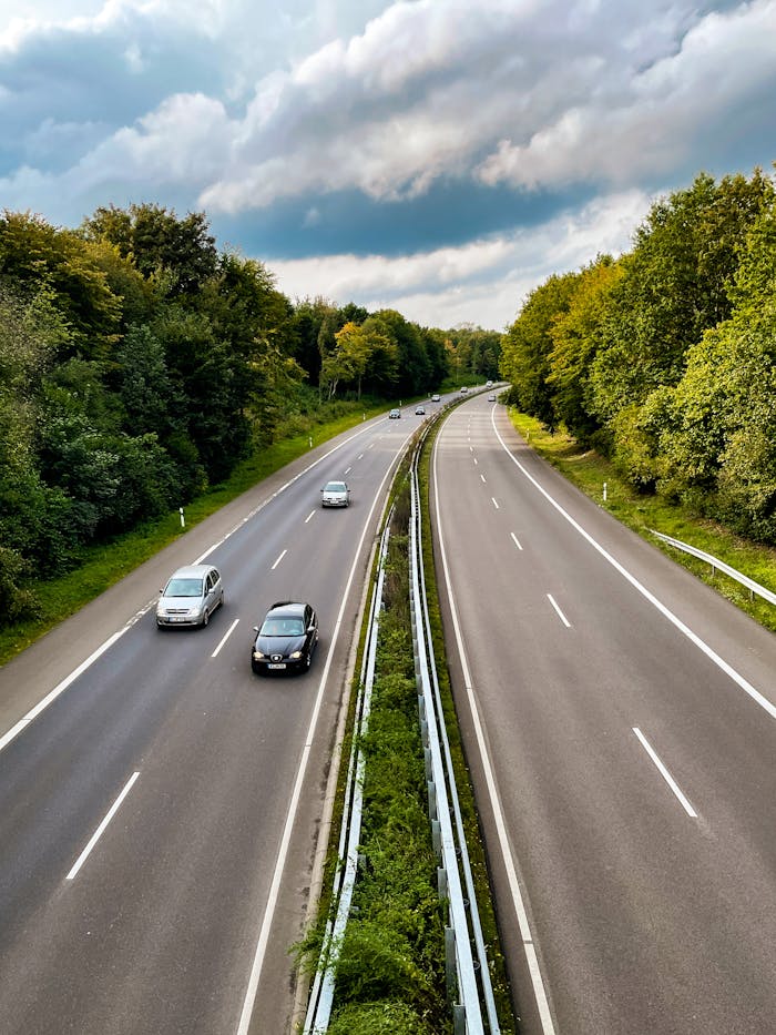 A peaceful highway scene with cars on an open road, flanked by lush green trees, under a cloudy sky.